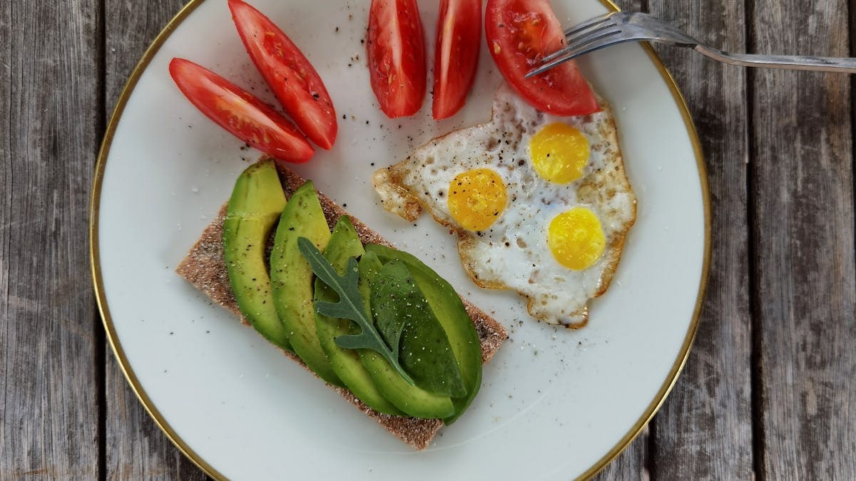 Delicious breakfast plate with sliced avocado, tomatoes, and sunny-side-up quail eggs.